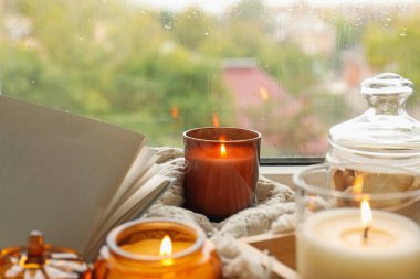 Yağmurlu bir günde pencere eşiğinde mum, kitap ve ekose yakmak, yakın çekim. Sonbahar atmosferi