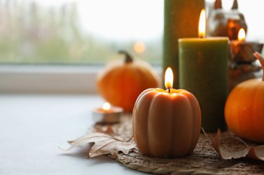 Yağmurlu bir günde pencere pervazında mum ve kuru yapraklar yakmak, yazı için yer açmak. Sonbahar atmosferi