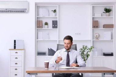 Ofisteki klimayı açmak için uzaktan kumanda kullanan bir adam.