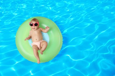Güneş gözlüklü, yüzme havuzunda şişme yüzük takan şirin bir bebek. Üst görünüm