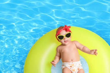 Güneş gözlüklü şirin bir bebek ve yüzme havuzunda sarı şişirilebilir bir yüzük. Üst görünüm