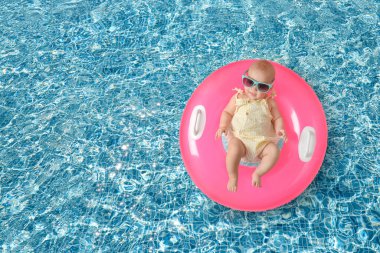 Güneş gözlüklü şirin bir bebek ve yüzme havuzunda pembe şişirilebilir bir yüzük. Üst görünüm
