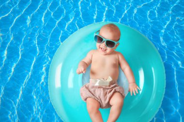 Güneş gözlüklü şirin bir bebek ve yüzme havuzunda pembe şişirilebilir bir yüzük. Üst görünüm