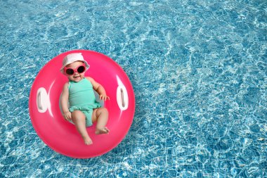 Güneş gözlüklü şirin bir bebek ve yüzme havuzunda pembe şişirilebilir bir yüzük. Üst görünüm