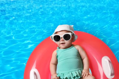 Güneş gözlüklü şirin bir bebek ve yüzme havuzunda pembe şişirilebilir bir yüzük. Üst görünüm