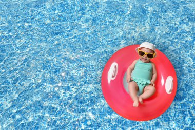 Güneş gözlüklü şirin bir bebek ve yüzme havuzunda pembe şişirilebilir bir yüzük. Üst görünüm