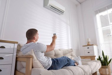 Evdeki kanepede uzaktan kumandalı bir adam klimayı açıyor.