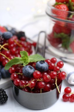 Olgun kırmızı frenk üzümü, yaban mersini ve nane yaprakları beyaz fayanslı masada kepçe halinde, yakın plan.