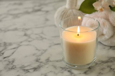 Beautiful spa composition with burning candle on white marble table, closeup. Space for text