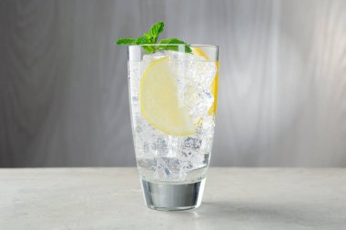 Açık gri masada limonlu, buzlu ve naneli taze su, yakın plan.