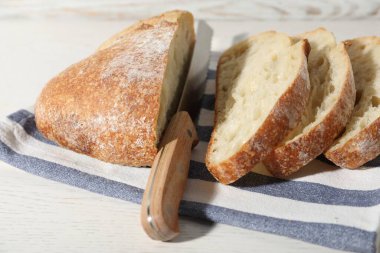 Beyaz ahşap masada bir somun taze ekmek ve bıçak, yakın plan.