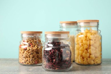 Açık mavi arka planda gri masada farklı ürünler bulunan cam kavanozlar