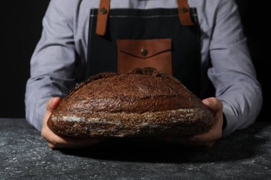 Gri desenli masada bir somun taze ekmekle fırıncı, yakın plan.