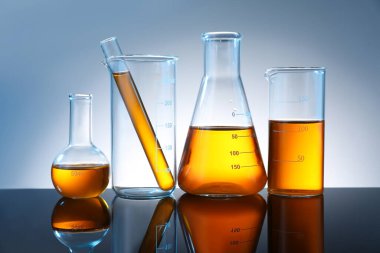 Ayna yüzeyinde gri arka planda turuncu sıvı bulunan farklı camlar.