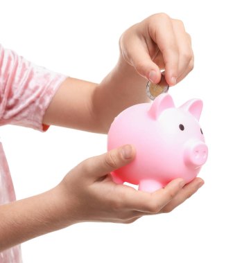 Küçük kız cep harçlığını beyaz arka planda kumbaraya yatırıyor.