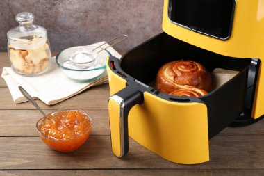 Fırında pişmiş tarçınlı çörekler, reçel, kurabiye ve un ahşap masada, gri arka planda, yakın planda.