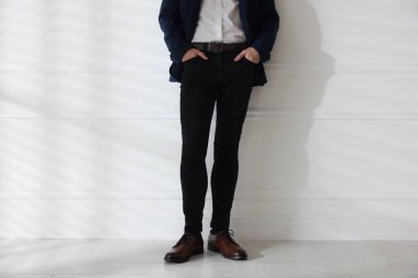 Beyaz duvarın yanında şık kotlu bir adam, yakın plan.