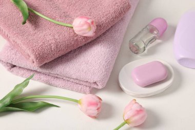 Temiz havlu yığını, kozmetik ürünler ve beyaz masa üzerinde lale çiçekleri.