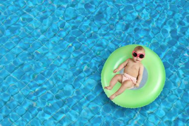 Güneş gözlüklü, yüzme havuzunda şişme yüzük takan şirin bir bebek. Üst görünüm