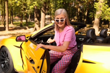 Güneş gözlüklü şık bir son sınıf öğrencisi modern Cabriolet 'ten dışarı çıkıyor.