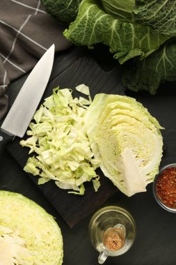 Cut fresh Savoy cabbage, spices, oil and knife on black table, flat lay