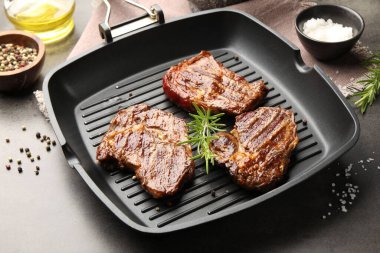 Izgara biftekli tava, biberiye ve baharatlar gri desenli masa, yakın plan.