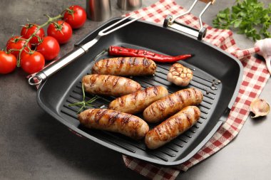 Izgara sosis, baharat ve domatesli tava gri desenli masa, yakın plan.