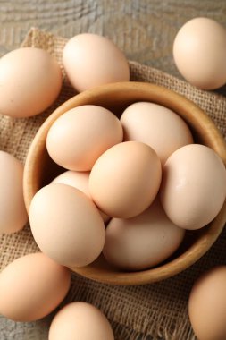 Raw chicken eggs in bowl on wooden table, flat lay
