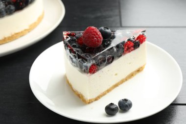Piece of delicious cheesecake with berries on black wooden table, closeup
