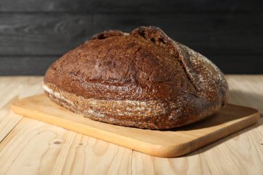 Hafif ahşap masada bir somun taze ekmek, yakın plan.