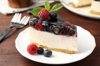 Bir parça lezzetli peynirli kek, böğürtlenli ve nane şekerli, ahşap masada servis ediliyor, yakın plan.