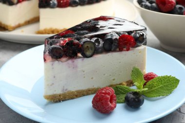 Piece of delicious cheesecake with berries and mint on grey table, closeup