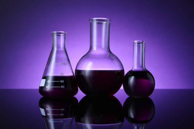 Masada mor arkaplana karşı renk sıvısı bulunan farklı bir laboratuar cam.