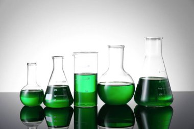 Masada beyaz arka plana karşı yeşil sıvı bulunan farklı bir laboratuar cam.