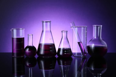 Masada mor arkaplana karşı renk sıvısı bulunan farklı bir laboratuar cam.