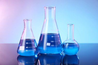 Ayna yüzeyinde mavi sıvı bulunan cam mataralar renk arkaplanına karşı