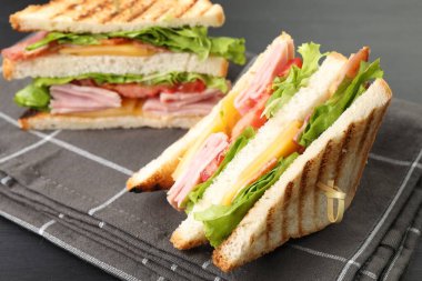 Jambonlu, pastırmalı, peynirli ve sebzeli lezzetli sandviçler siyah ahşap masada, yakın plan.