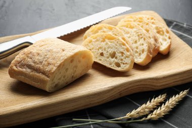 Taze ciabatta parçaları, siyah masada bıçak ve buğday kulakları, yakın plan.