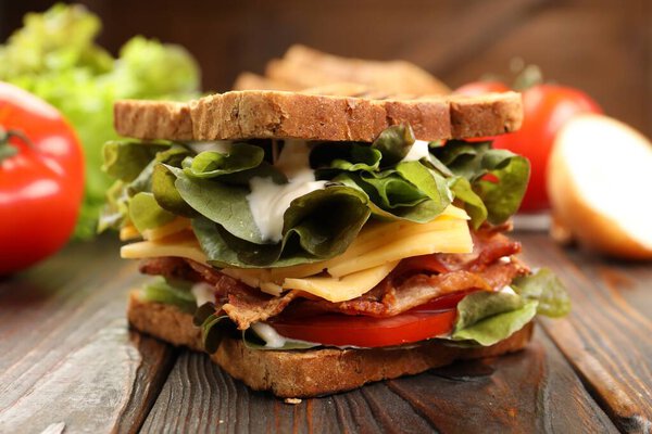 Вкусный сэндвич с беконом, сыром, овощами и соусом на деревянном столе, крупным планом
