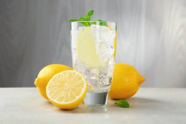 Limon meyveli ferahlatıcı su, açık gri masada buz ve nane, yakın plan.