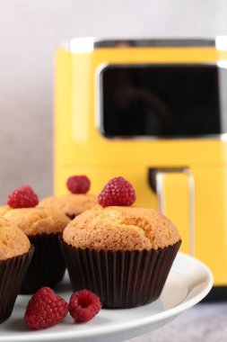 Kürsüde ahududulu enfes fırınlanmış kekler ve gri arka planda hava fritözü, seçici odak