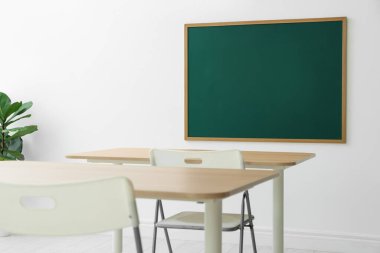 Boş yeşil karatahta, masalar, sandalyeler ve bitkiler sınıfta