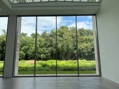 Güzel yeşil ağaçlar ve mavi gökyüzünün altındaki diğer farklı bitkiler, panoramik pencerelerden bakıyorlar.