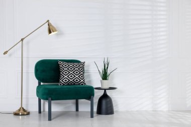 Şık lamba, yastıklı rahat koltuk ve beyaz duvarın yanındaki bitki örtüsü.