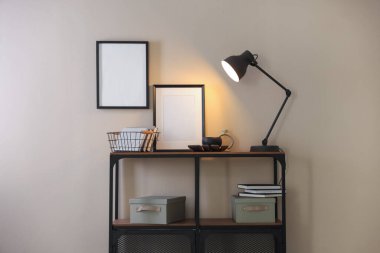 Stylish lamp, other decor and books on console table near beige wall indoors