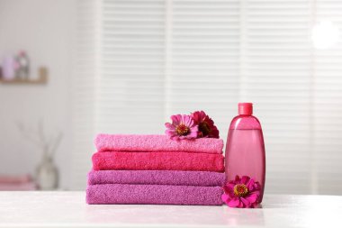 Beyaz masa üzerinde temiz havlu, çiçek ve kozmetik ürünler yığını.