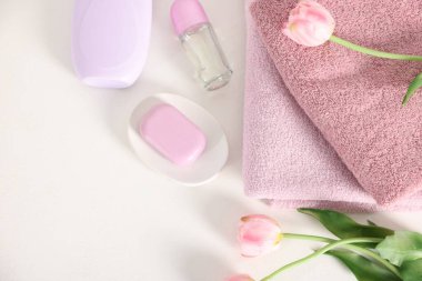 Bir yığın temiz havlu, kozmetik ürünler ve beyaz masa üzerinde lale çiçekleri.