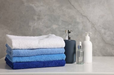 Gri arka plana karşı beyaz masada bir yığın temiz havlu ve kozmetik ürünler.