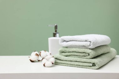 Yığınla temiz havlu, pamuk çiçeği ve kozmetik ürünü yeşil arka plana karşı beyaz masada.