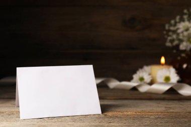 Boş kart, çiçekler, kurdele ve yanan mum ahşap masada, yakın plan.